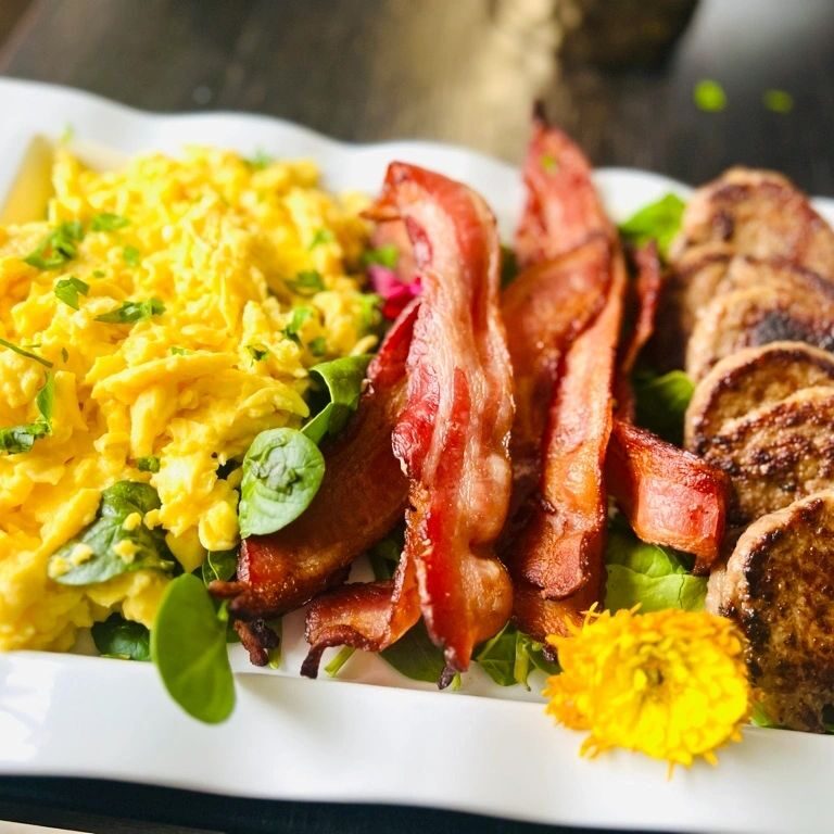 Scrambled eggs, bacon, sausage on white plate.